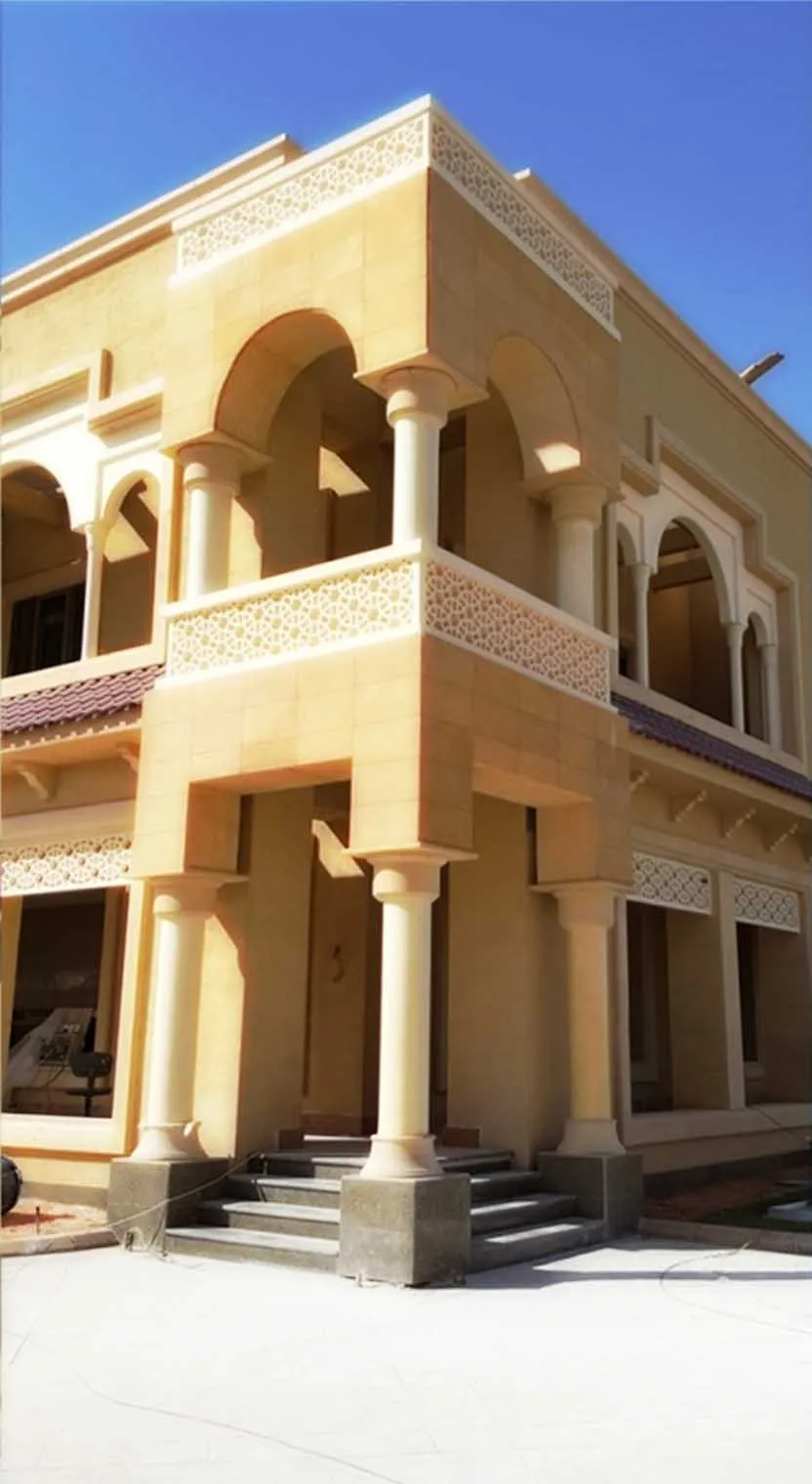Stone-clad palace elevation in Riyadh — carved arches, turned columns and a pierced screen balustrade in warm limestone against a hard blue sky