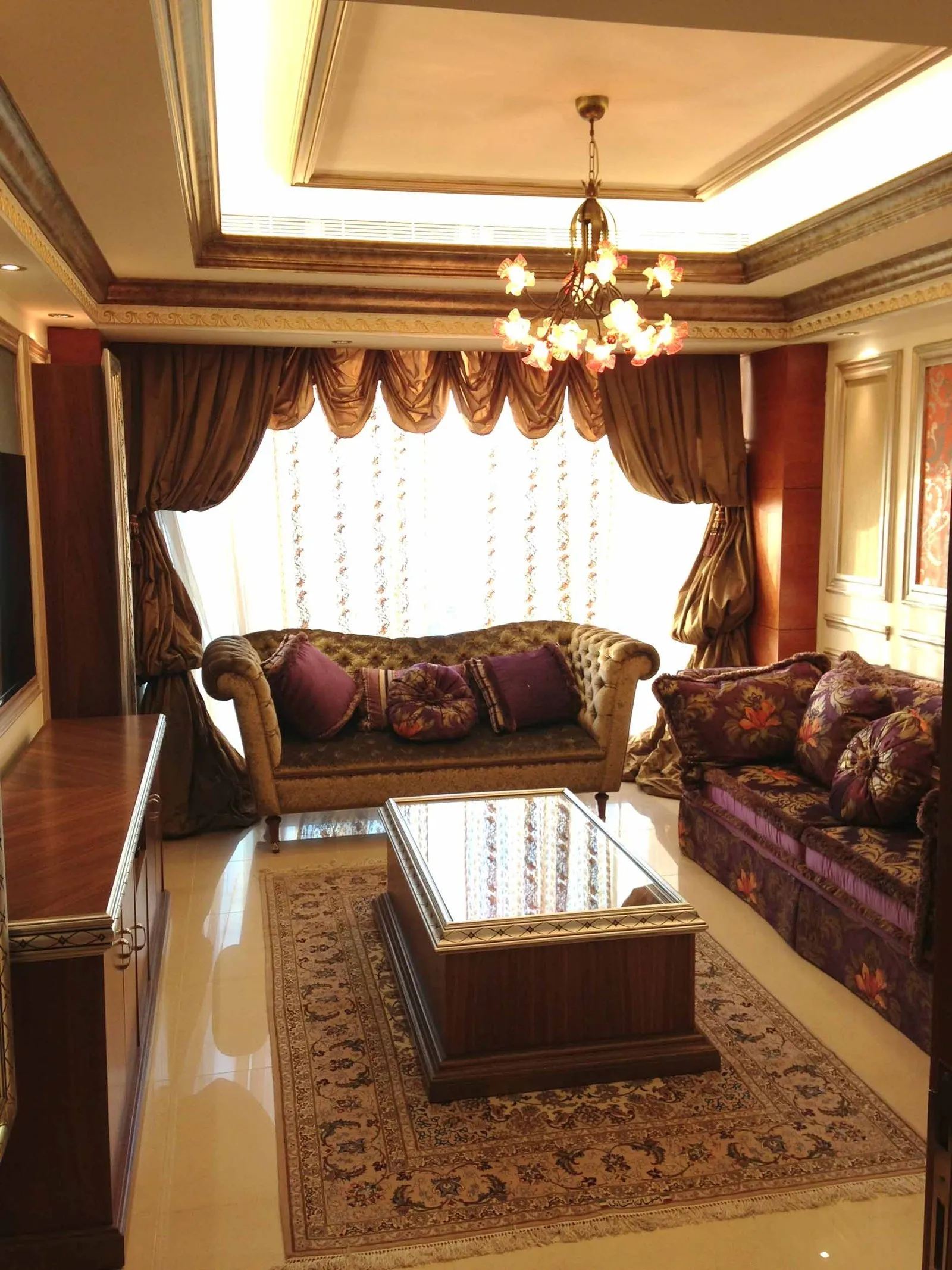 Sitting area with tufted chesterfield sofas in gold and purple velvet, patterned cushions and layered floral-patterned rugs