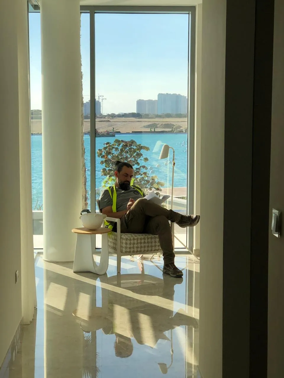 Samer Najjar seated in a glazed interior overlooking a waterfront development under construction, reviewing project drawings